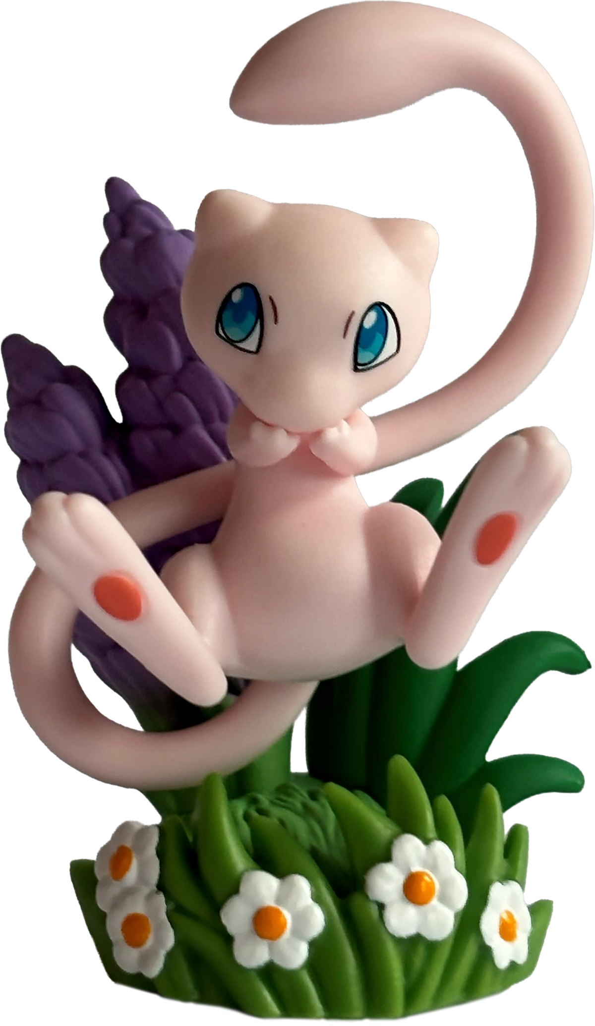 Pokémon Mew-Figur auf grünem Gras mit Blumen und ausgestrecktem Schwänzchen